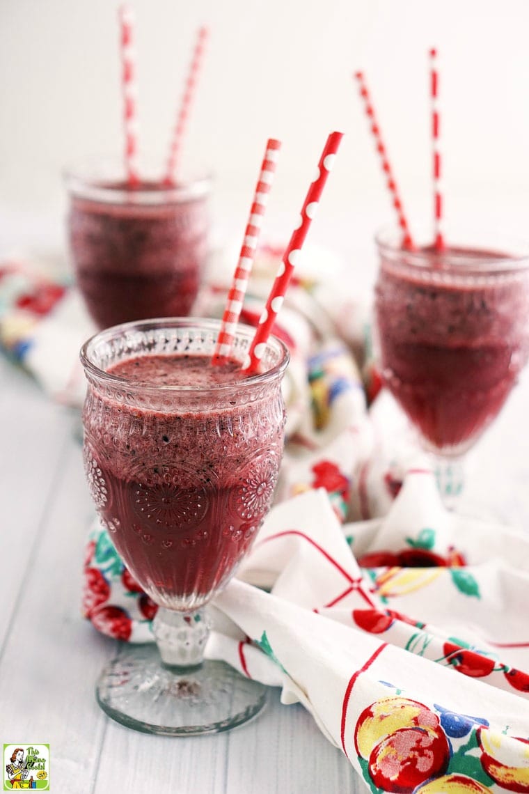 Three glasses of berry smoothies with red straws on a vintage tablecloth.