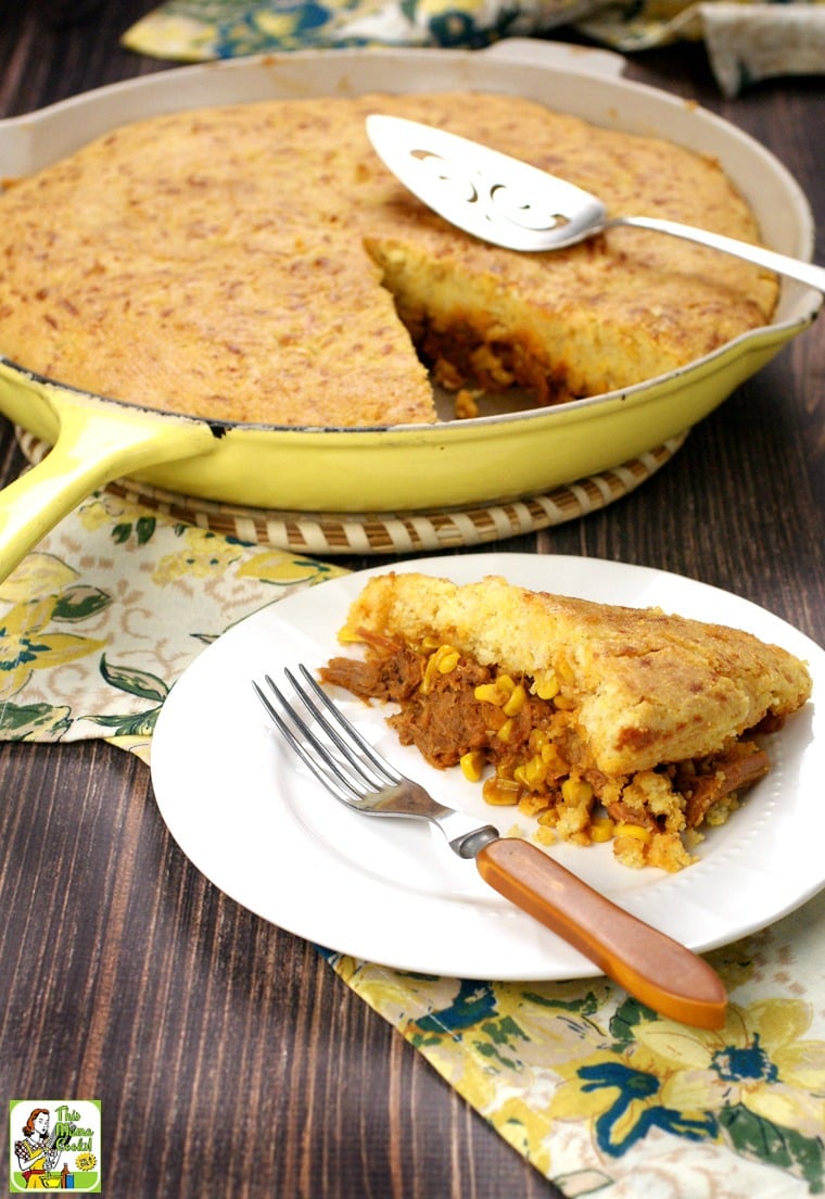 A slice of Pulled Pork Skillet with Cornbread on a white plate with a fork with a yellow skillet in the background.