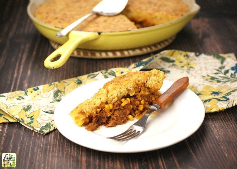 A white plate of Pulled Pork Skillet with Cornbread with a fork and napkin with a yellow skillet in the background.