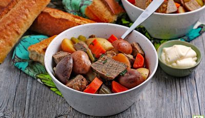 Slow Cooker Venison Stew in a white bowl with a spoon next to a small bowl of horseradish and rolls of crunchy bread.