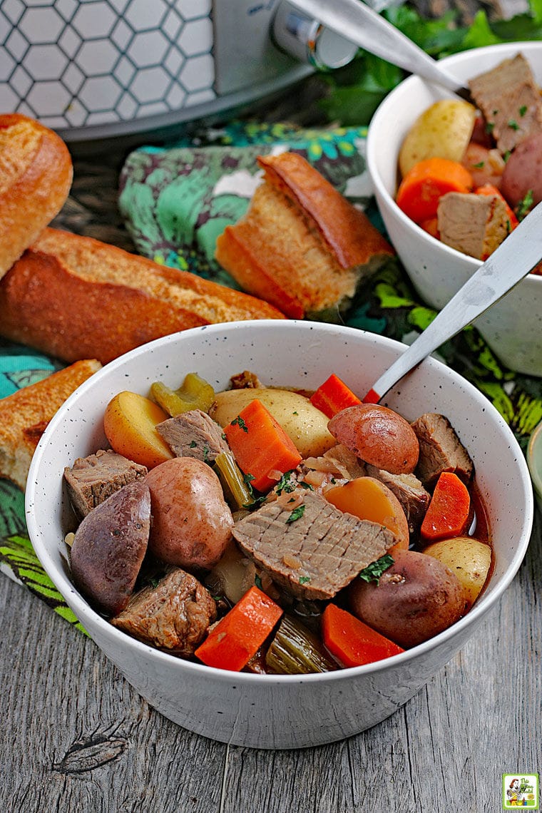 Closeup of a bowl of crockpot venison stew with pieces of French bread in the background.
