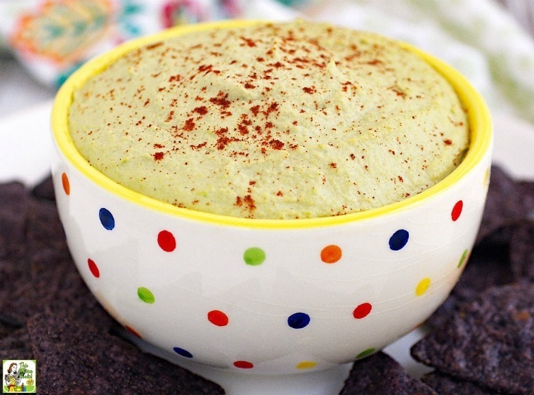 A polka dotted bowl of Easy Edamame Hummus with blue tortilla chips.