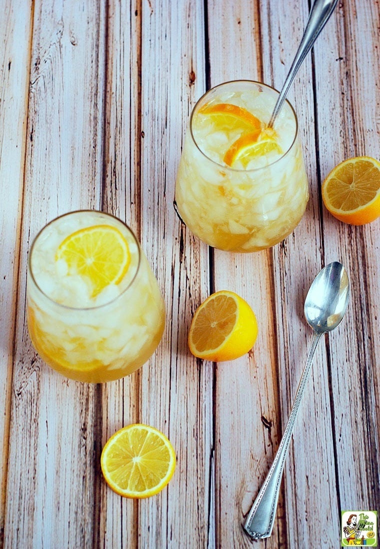 Overhead of two glasses of lemon shrub cocktails with sliced lemons and spoons. 