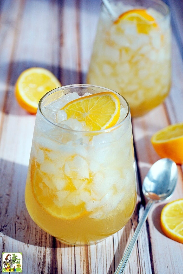 A cocktail glass of Meyer lemon shrub drink with sliced lemons and spoons. 