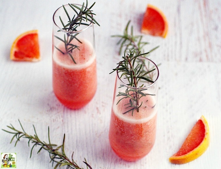 Glasses of Pink Greyhound Cocktails with sprigs of rosemary and slices of pink grapefruit.