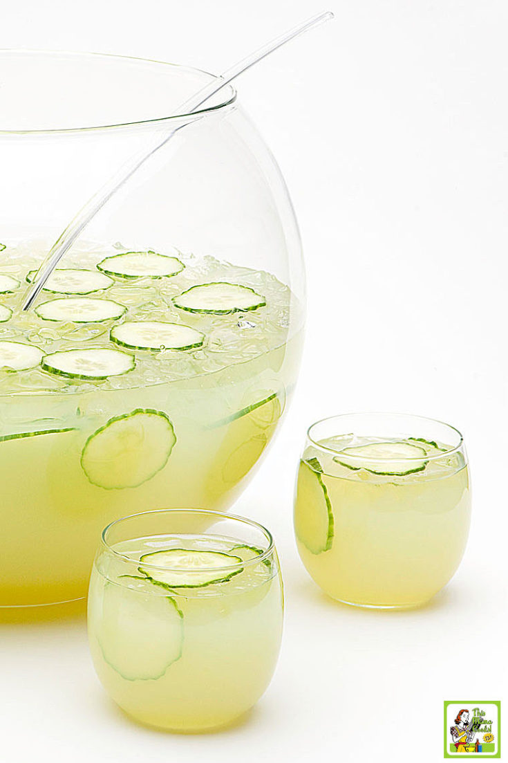 Sparkling Green Sangria in a punch bowl and in two cocktail glasses with sliced cucumbers and grapes.