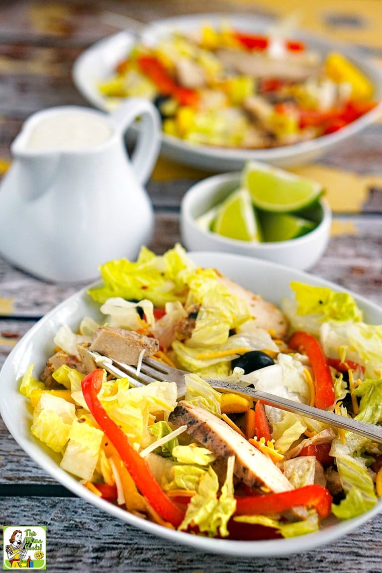 A bowl of Chicken Fajita Salad with limes and salad dressing in the background.