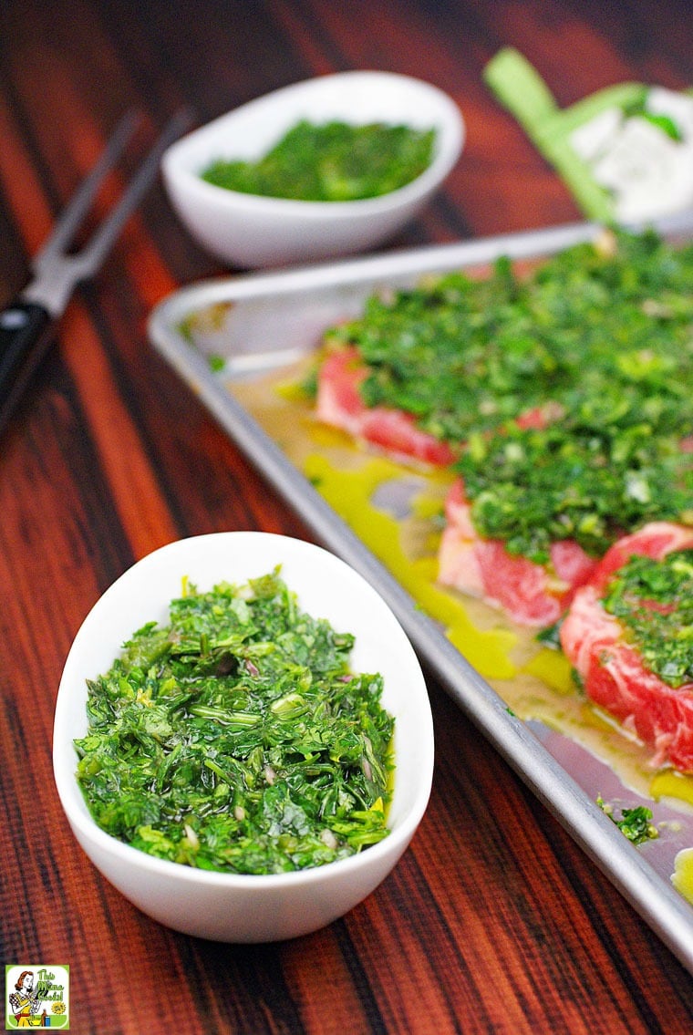 A bowl of chimichurri sauce and a a tray of chimichurri steak to be cooked with another bowl in the background.