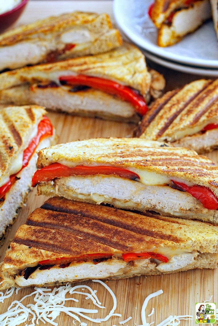 Chicken panini sandwiches on a wooden cutting board with shredded cheese.