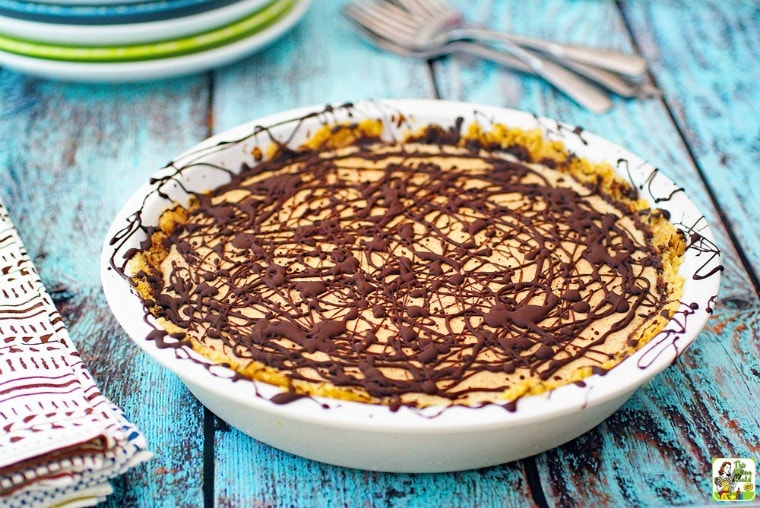 White pie plate with a No Bake Almond Butter Pie with forks, plates, and a cloth napkin.