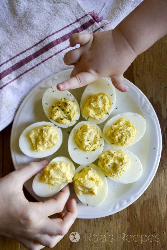 Hands grabbing Sour Cream & Sriracha Deviled Eggs off a plate.