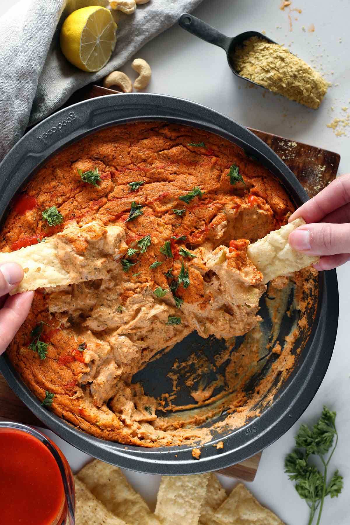 Hands dipping chips into a bowl of Vegan Jackfruit Buffalo Dip.