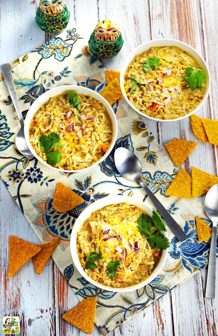 Overhead view of bowls of Slow Cooker Creamy Verde Chicken Chili with chips and serving spoons.