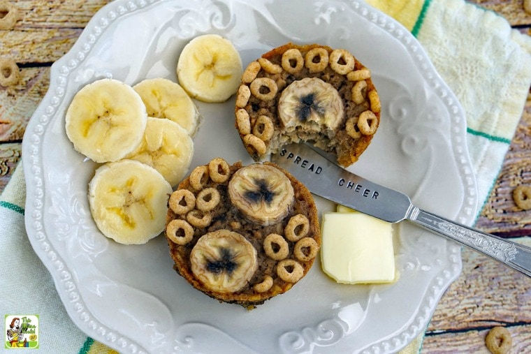 A gluten free banana muffins recipe on a white plate with banana slices, a pat of butter, and a knife next to a napkin.