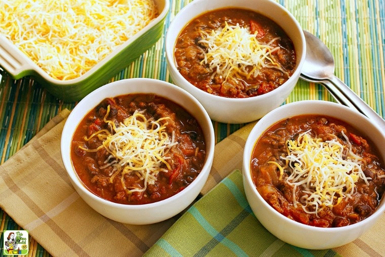 Three white bowls of turkey pumpkin chili with beans covered with shredded cheese