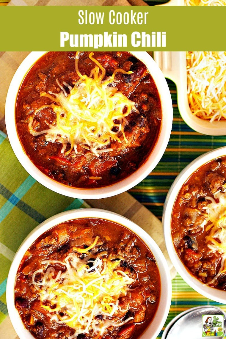 Three bowls of Slow Cooker Pumpkin Chili with shredded cheese on a plaid napkin and bamboo mat.