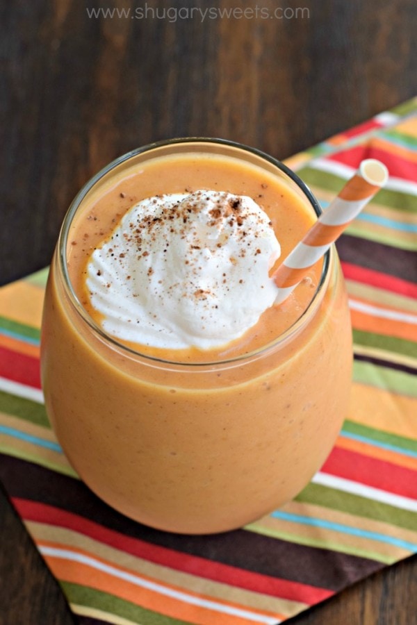 Pumpkin Pie Smoothie in a glass with a dollop of whipped cream and an orange striped straw.