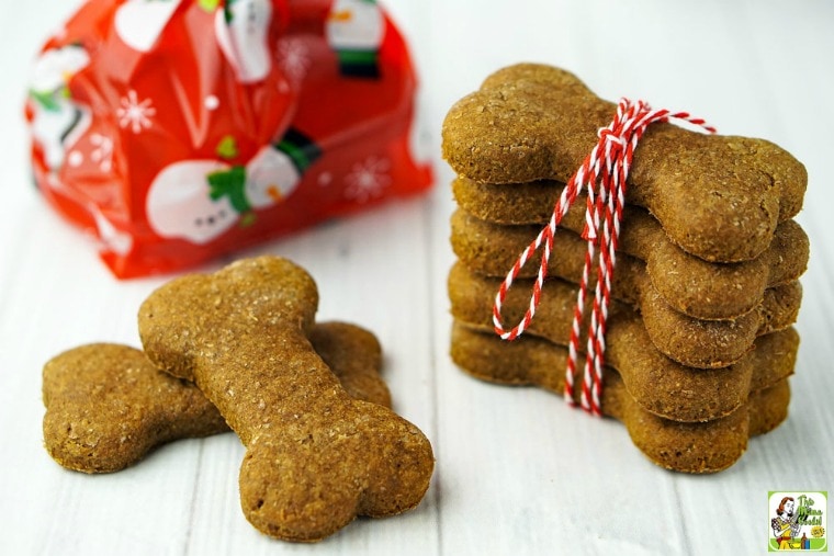 A pile of homemade dog treats wrapped in string, a couple more of dog biscuits with a festive holiday gift bag in the background.