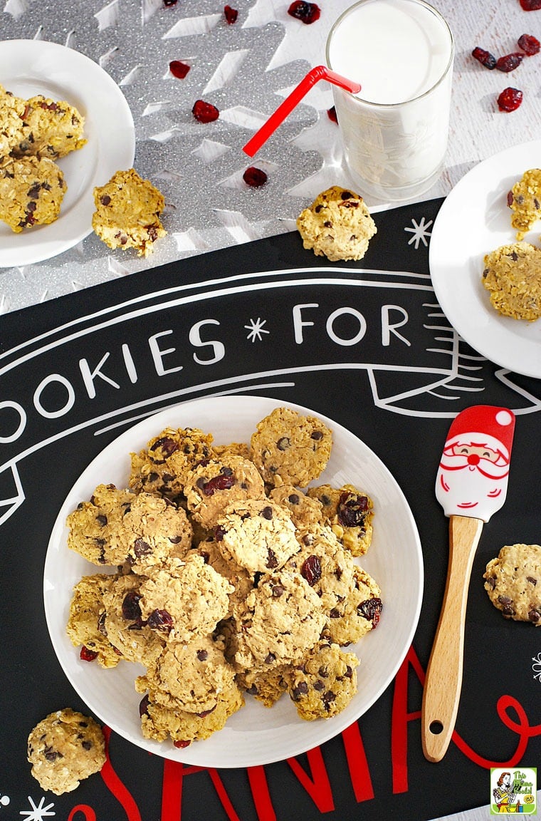 Cookies for Santa placemat with a plate of gluten free oatmeal cookies with chocolate chips and raisins, a glass of milk with a straw, and a Santa spatula.