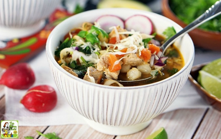 A bowl of pozole soup with radishes, cabbage, and limes with spoon.