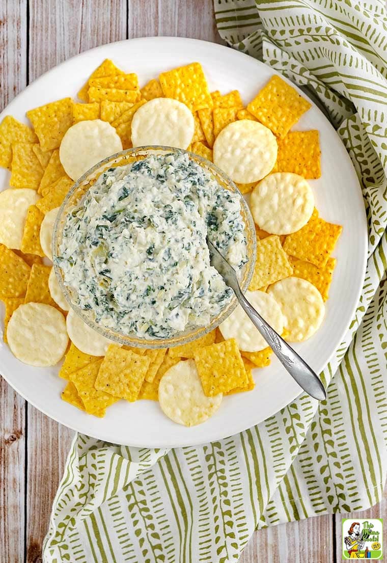 A white plate of crackers spread with Vegan Spinach Artichoke Dip and a serving knife.