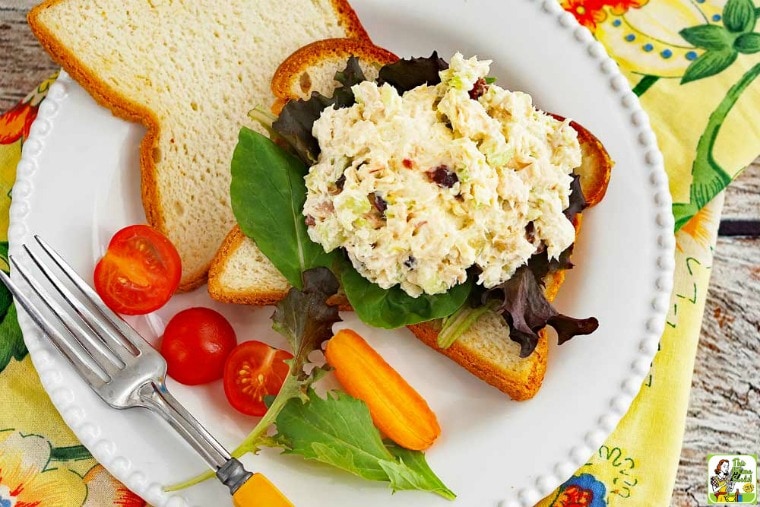 Easy rotisserie chicken salad sandwich on a white plate with tomatoes and carrot, fork, and colorful napkins.