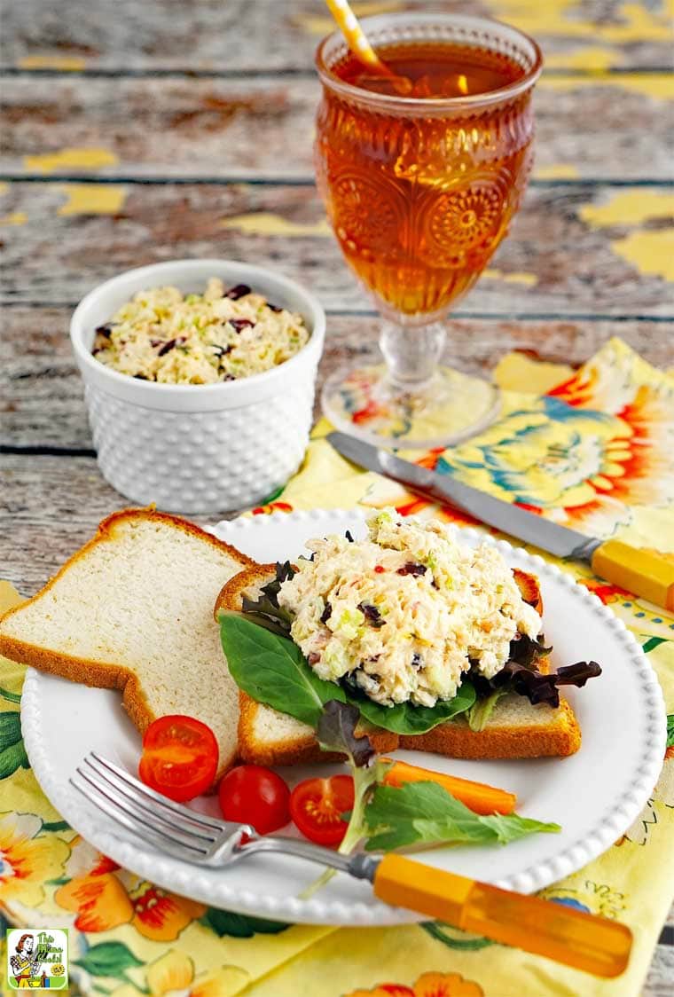 Easy Chicken Salad Sandwich on a plate with tomato, lettuce, cutlery, and a glass of iced tea