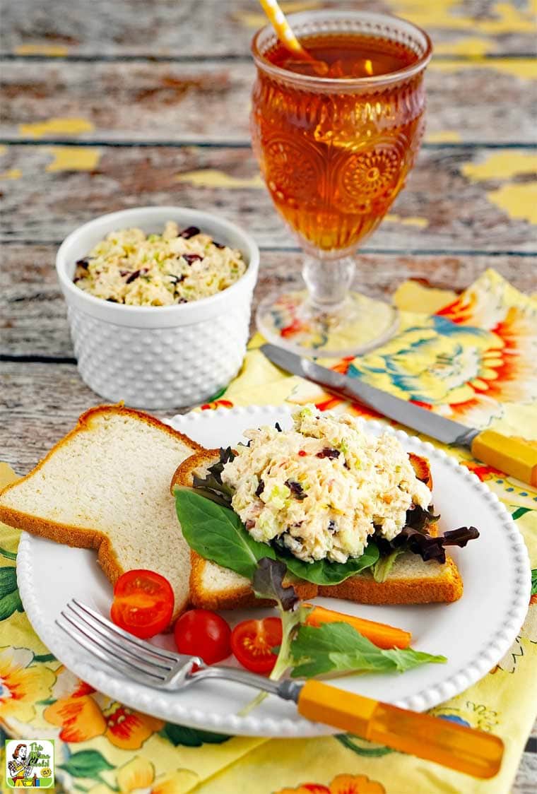 Rotisserie chicken salad sandwich on a plate with tomato, lettuce, cutlery, and a glass of iced tea