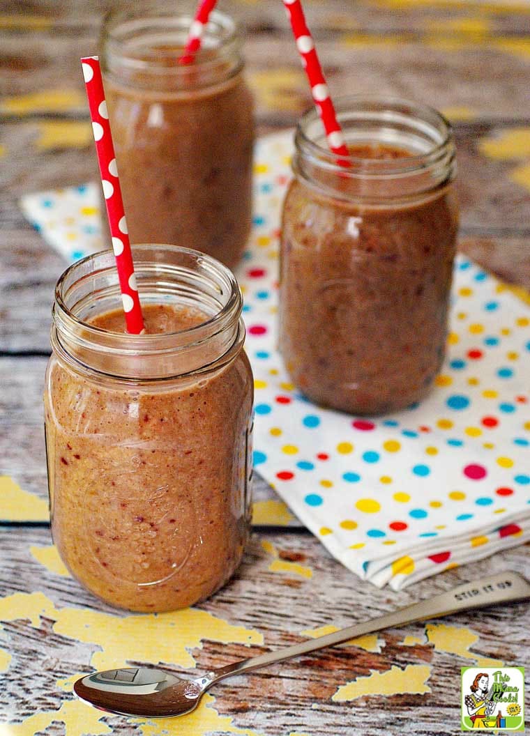 Three jars of oatmeal smoothies in a mason jars with red straws with a polka dot tea towel with an ice tea spoon.