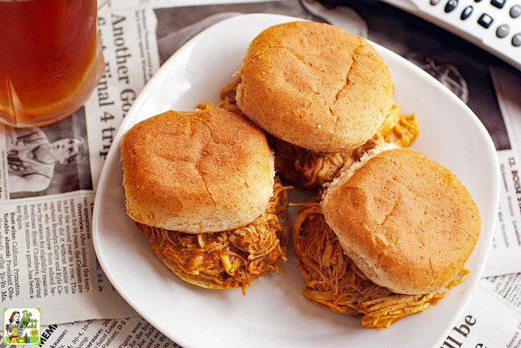 A white plate of Buffalo Chicken Sliders, a glass of beer, and a TV remote.