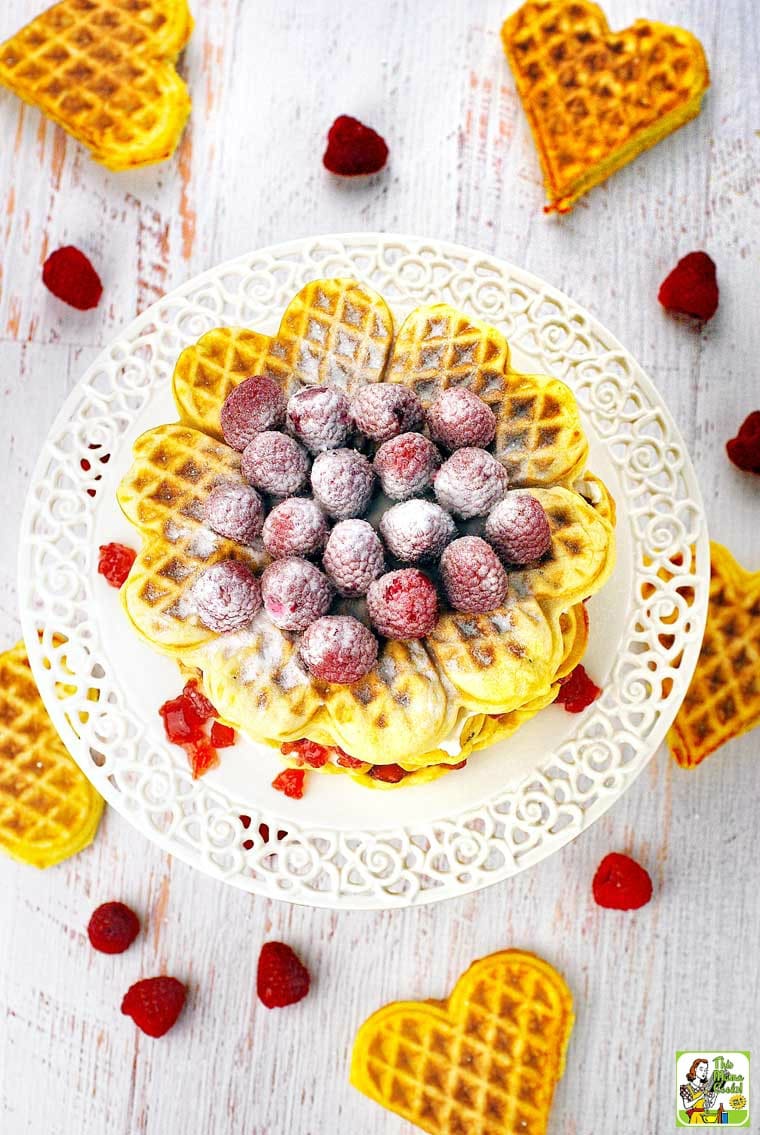 Overhead shot of a waffle cake with sugared raspberries on a white cake stand.