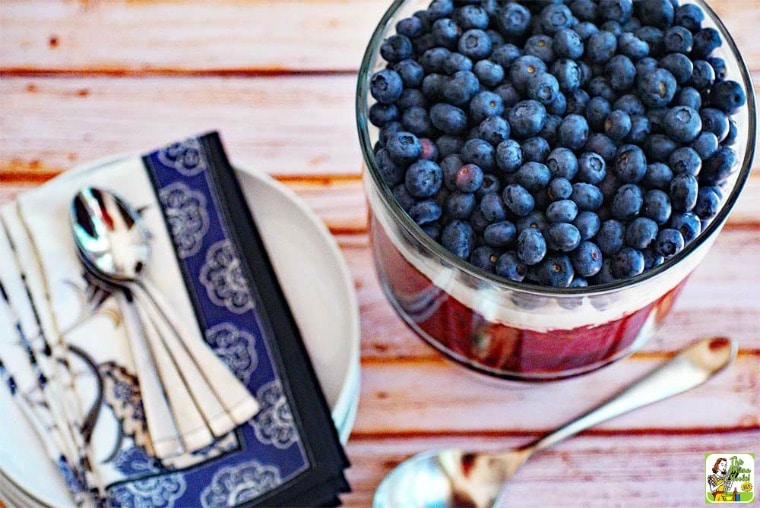 Red White and Blue Trifle with blueberries and whipped cream in a glass trifle bowl with blue napkins and serving spoons.