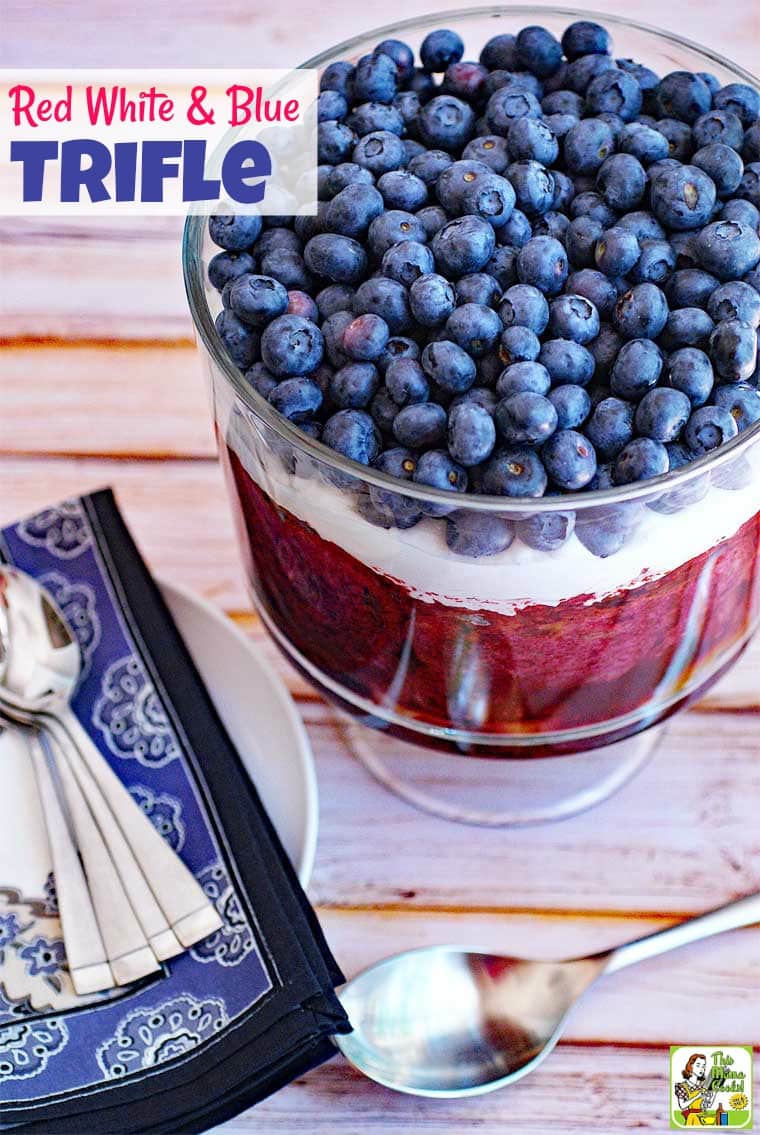 Red White and Blue Trifle with blueberries and whipped cream in a glass trifle bowl with blue napkins and spoons.