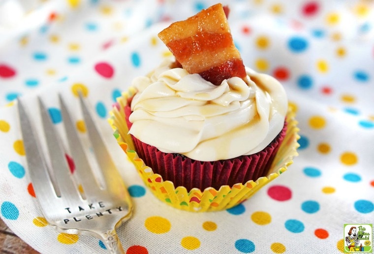 A bacon maple cupcake in colorful cupcake liners on a dotted tablecloth with a serving fork.