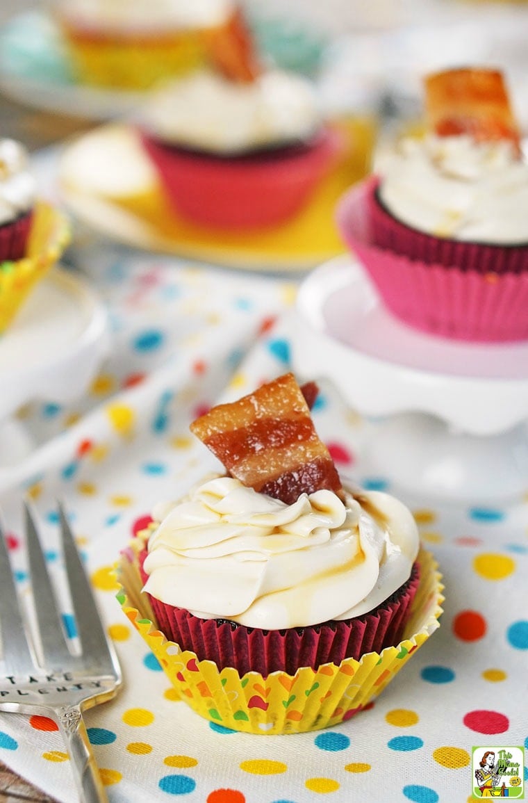 Bacon maple cupcakes with chocolate garnished with candied bacon on a polka dot tablecloth.