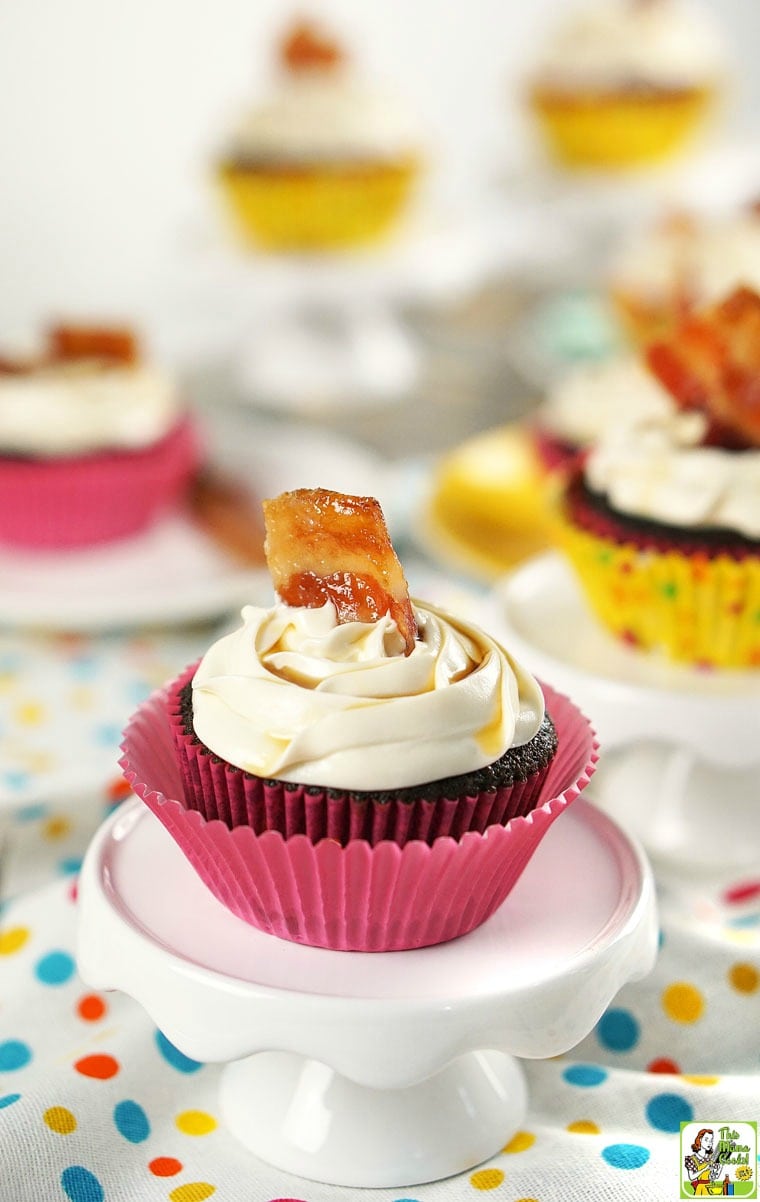 A chocolate maple bacon cupcake garnished with candied bacon on a mini cake stand on a polka dot tablecloth.
