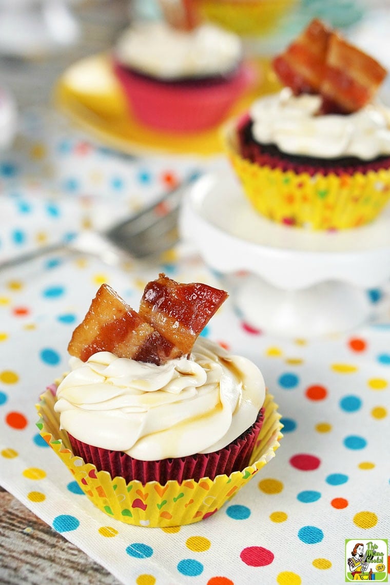 Chocolate cupcakes with vanilla frosting garnished with candied bacon on a polka dot tablecloth.