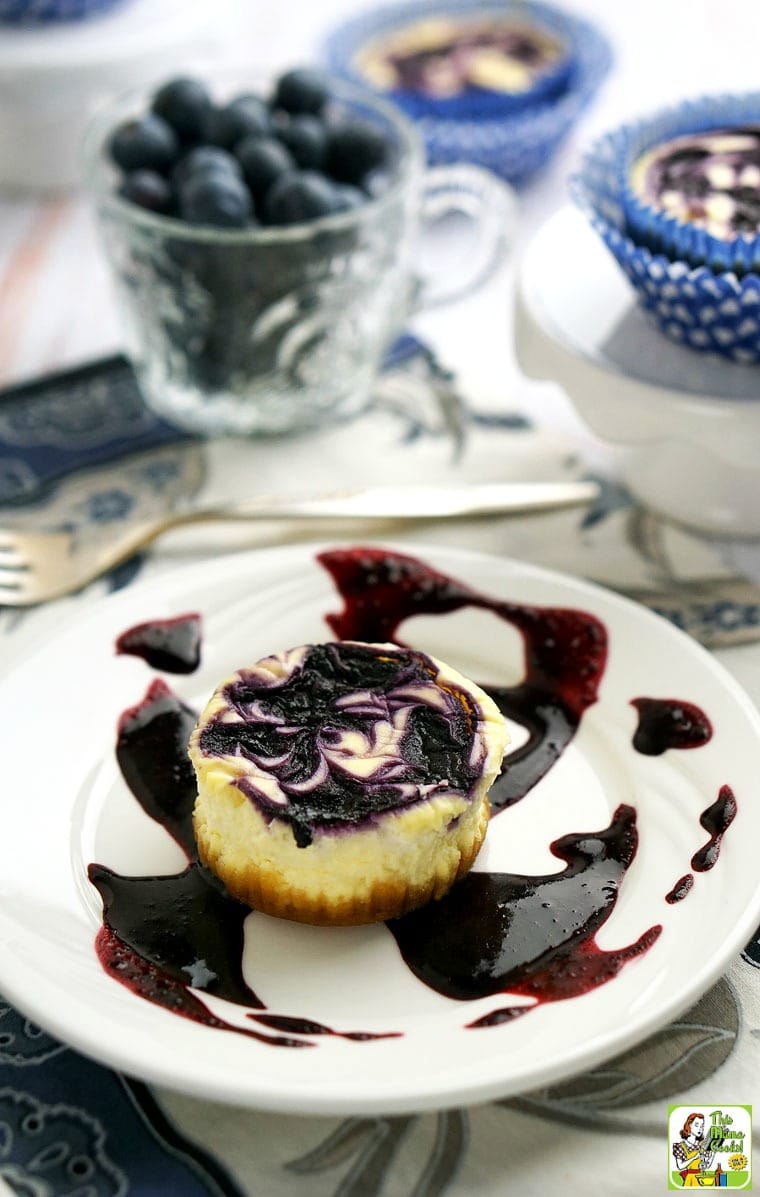 Mini cheesecake cupcake on a white plate with swirl of blueberry sauce.
