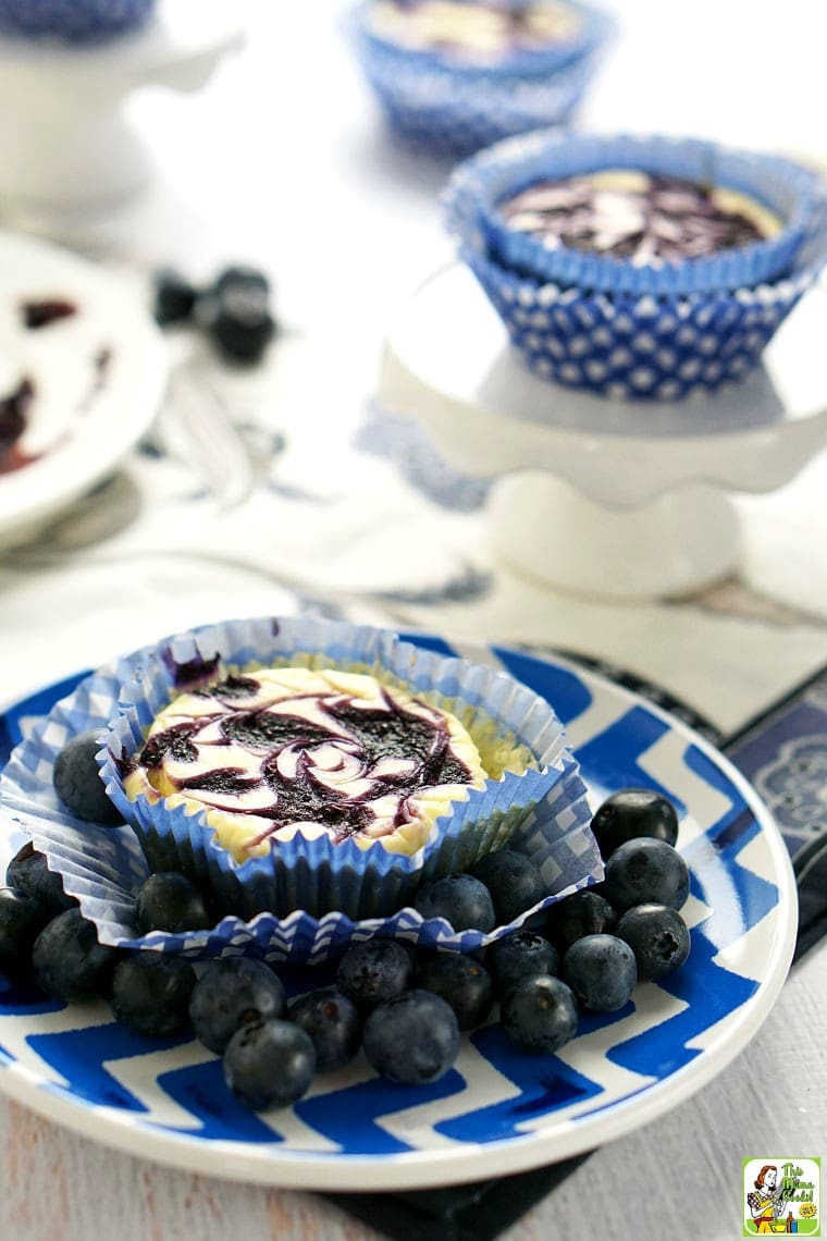 Mini cheesecake cupcake with blueberry sauce on a plate of blueberries.