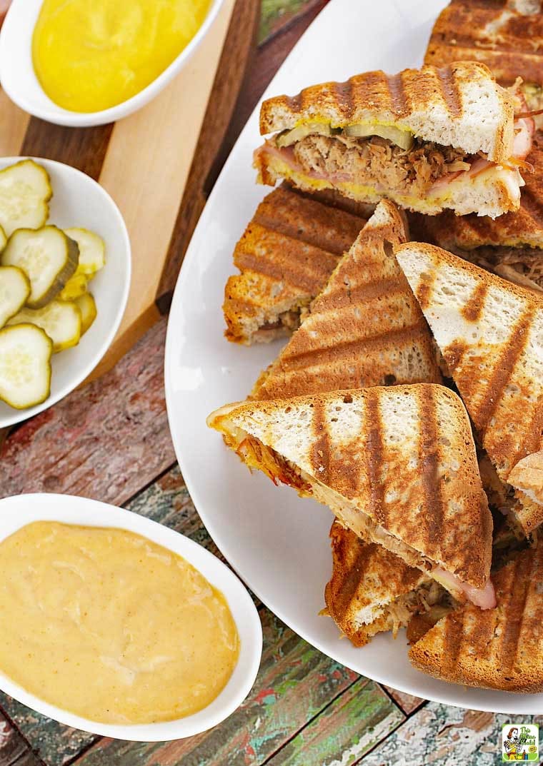 A platter of Cuban Paninis with mustard, pickles and dressing.