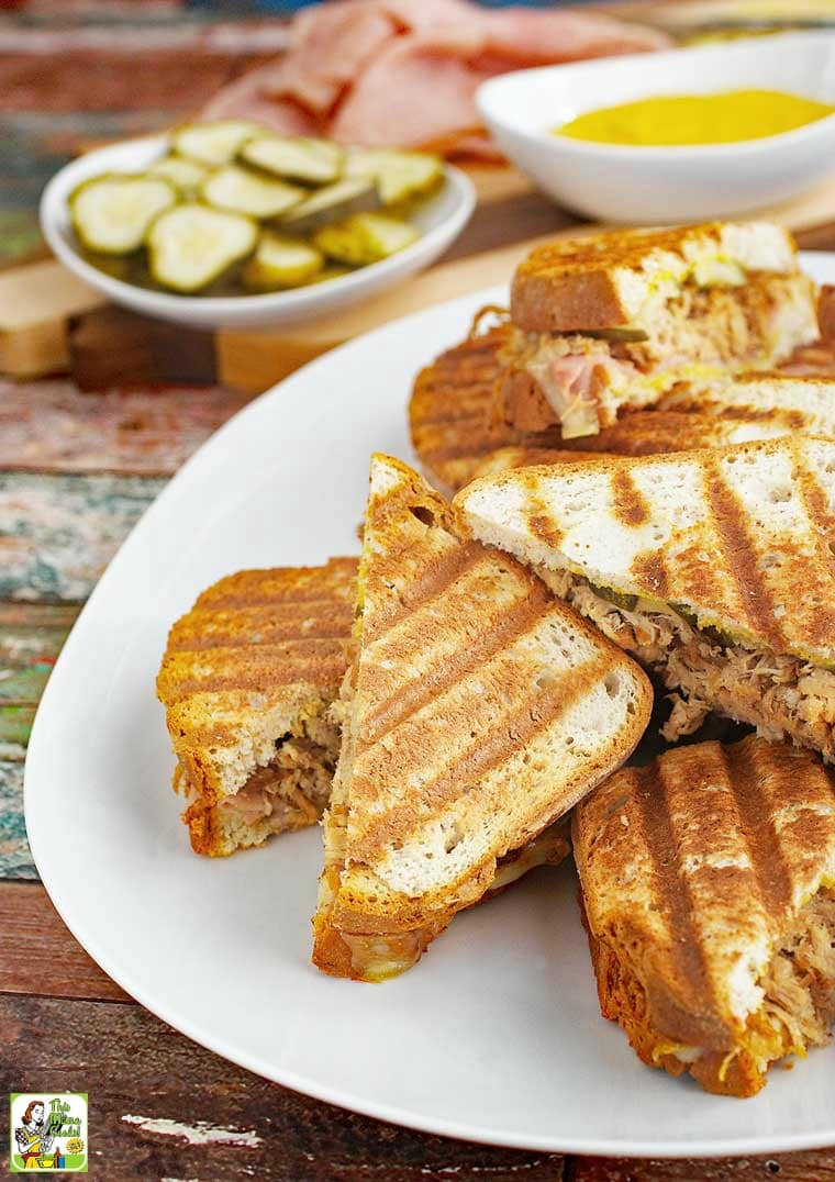 A platter of Cuban Paninis sandwiches with mustard and pickles.