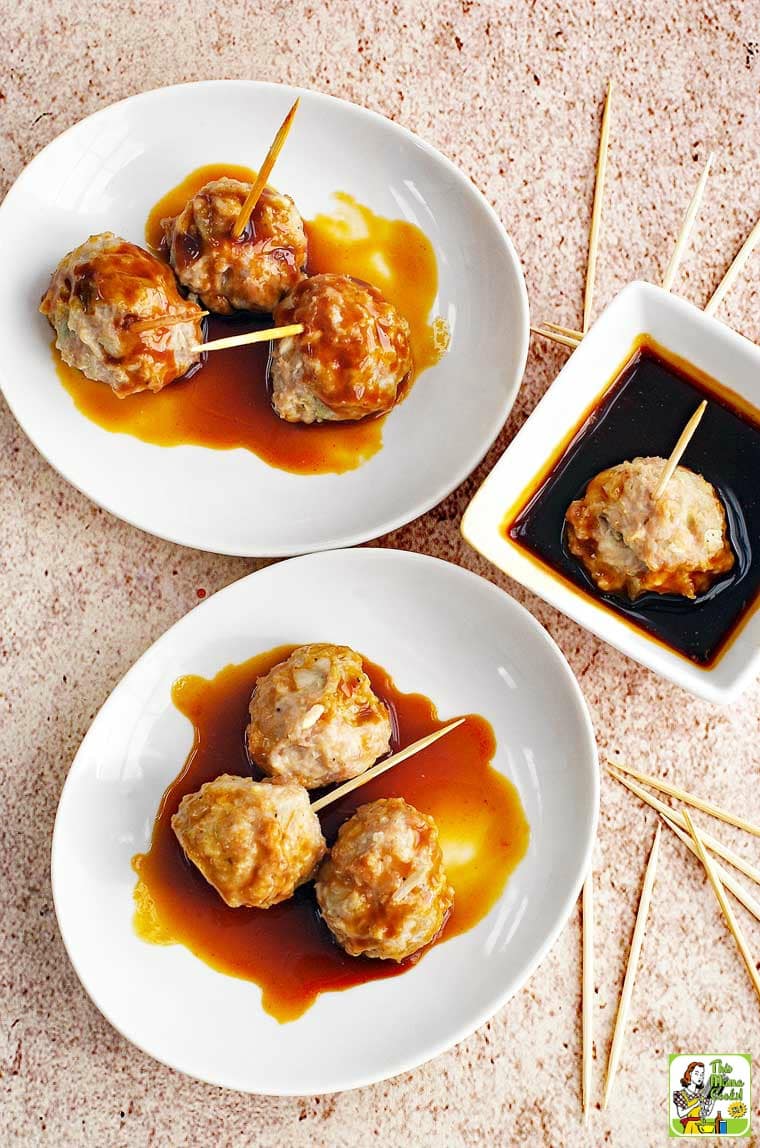 A bowl and plate of Asian style pork meatball appetizers served on toothpicks with a small bowl of dipping sauce. With extra toothpicks.