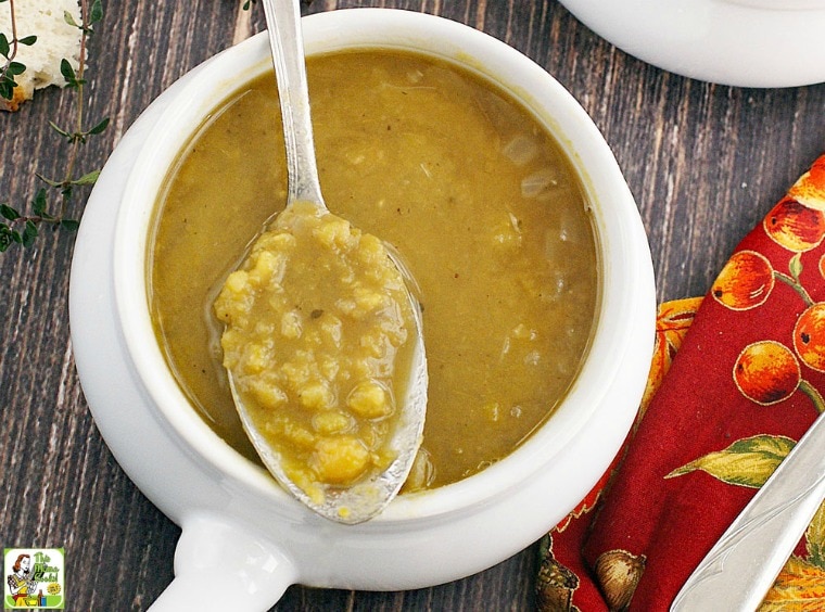 A lug handled bowl of split pea soup with spoon and colorful napkin.