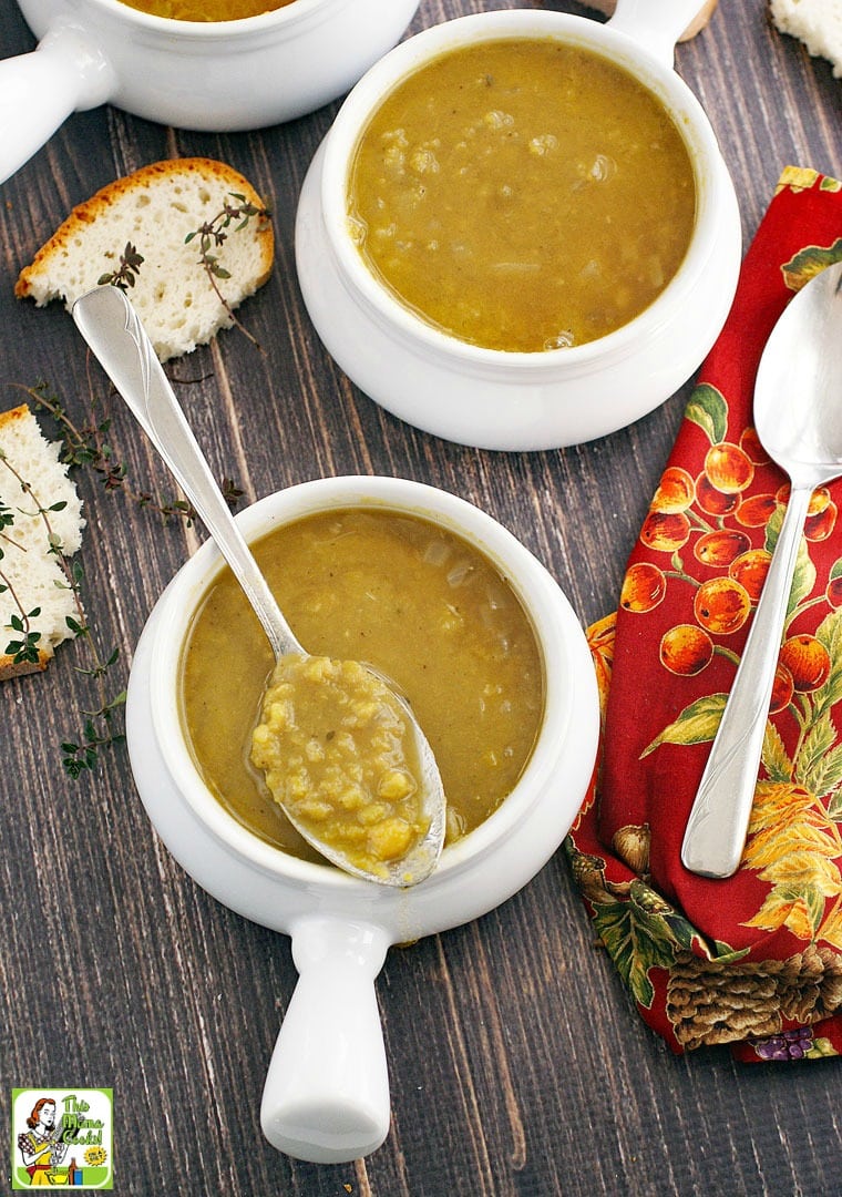 Overhead shot of green pea soup in white soup bowls with lug handles, soup spoons, red napkins, sprigs of thyme, and pieces of bread.