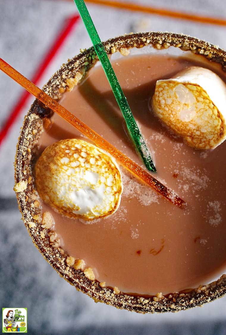 Overhead closeup of S'mores Martini served with toasted marshmallows and cocktail stirrers with glass rimmed with cookie crumbs.