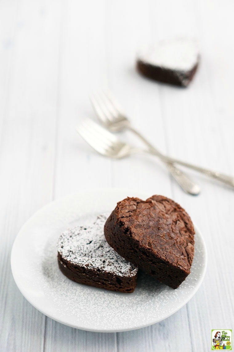 A white plate with two heart shaped brownies with forks and another brownie in the background.