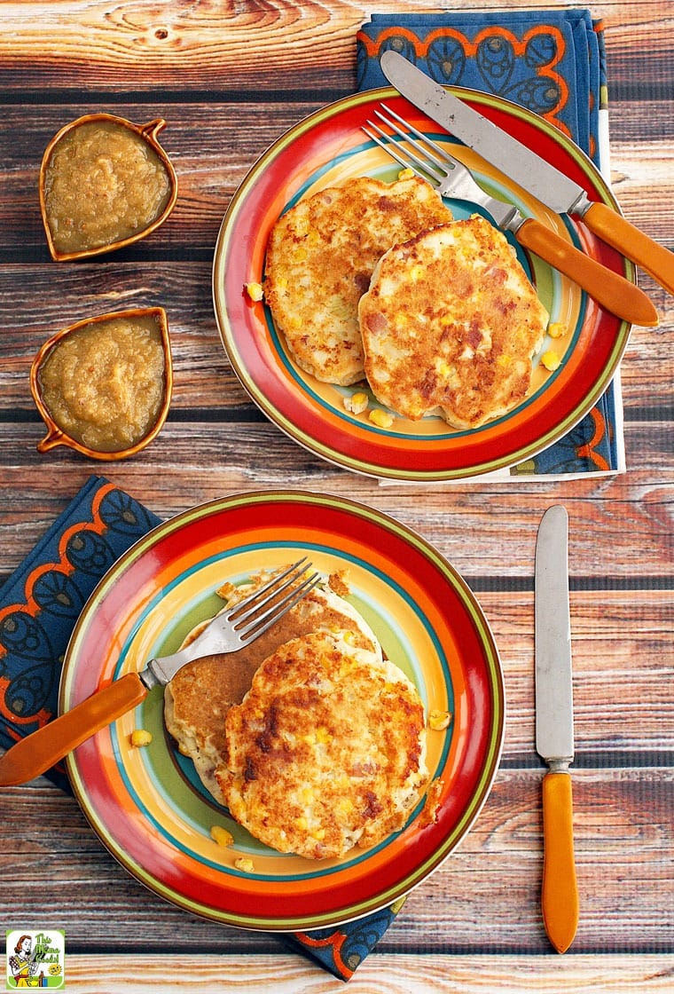 Corn fritters on a striped plates with a forks, knives and napkins and bowls of apple sauce.