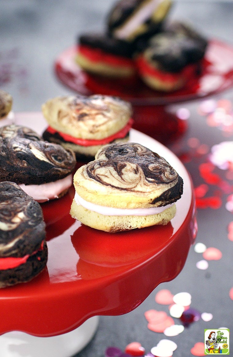 Chocolate and vanilla heart shaped whoopie pies on a red cake stand.
