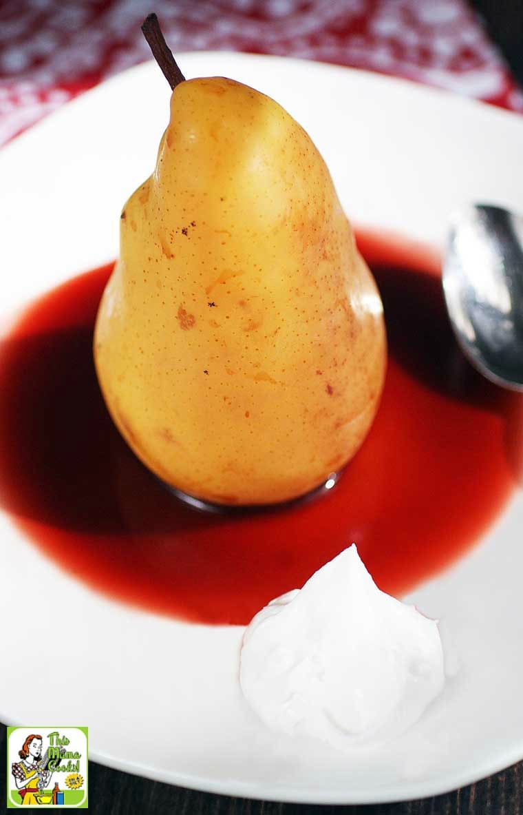 Closeup of a Poached Pear in cherry sauce with a dollop of coconut whipped cream with a spoon.
