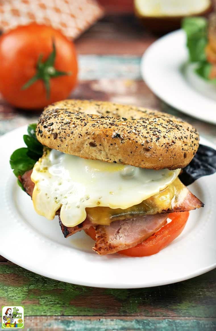 An egg, ham and cheese bagel sandwich on a white plate.